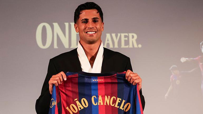 Joao Cancelo holds a Barcelona shirt with his name on after joining the club on a permanent contract in August 2026
