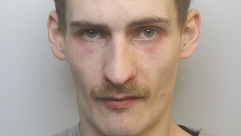 A custody picture of Daniel Gunter, who has dark blonde hair and a blonde moustache. He is looking at the camera with a serious expression and has dark red patches under his eyes.