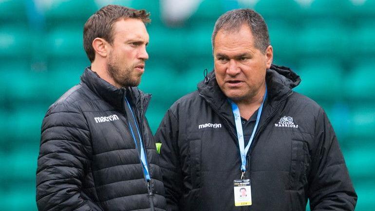 Mike Blair and Dave Rennie stand together in dark Glasgow Warriors coats, with both men having identity lanyards hanging from their necks