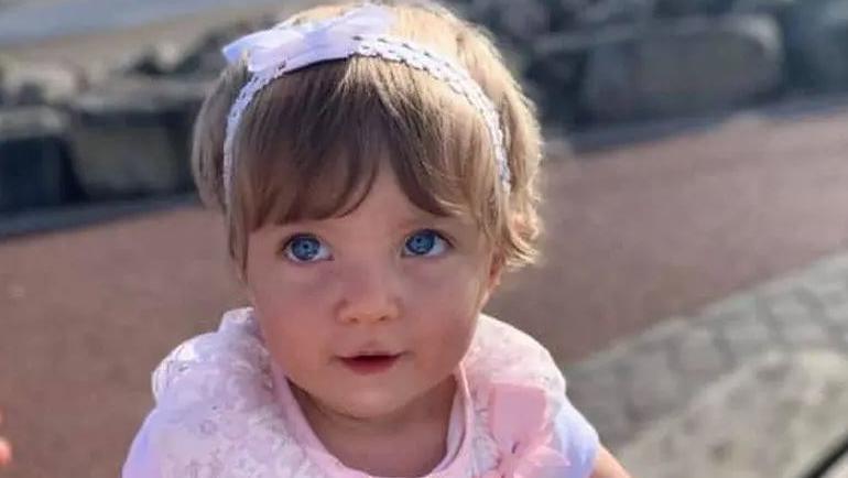 Little girl wearing a band in her hair and pink top looks up to the camera