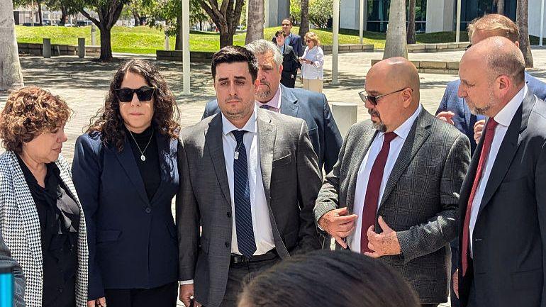 Dillon Angulo wears a grey suit and blue tie with people beside him