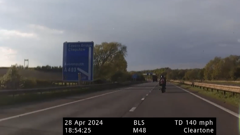 A motorcyclist in the outside lane of a dual carriageway with a speed gun readout underneath showing 140mph