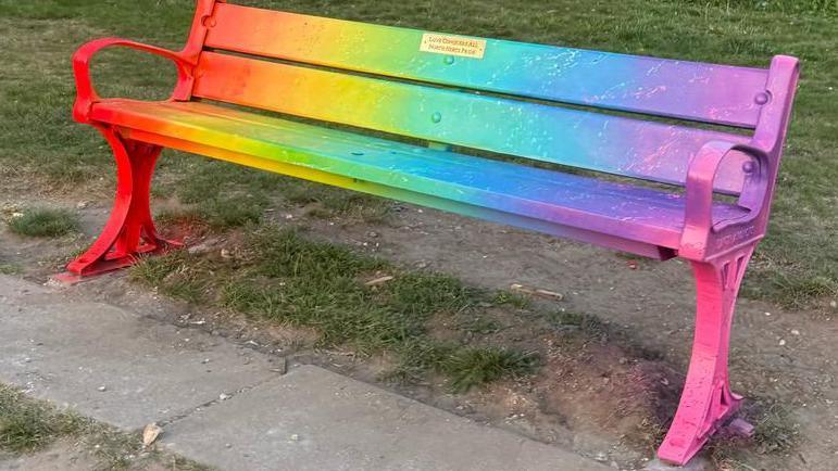 A park bench painted in different colours including yellow, pink and orange.
