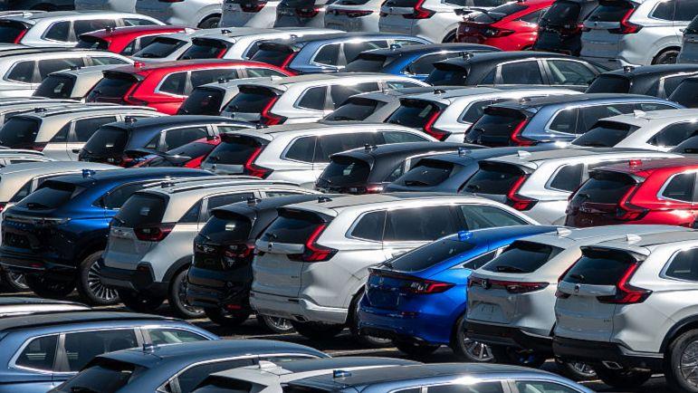 Red, blue, red and silver cars are lined up in rows in a huge carpark.