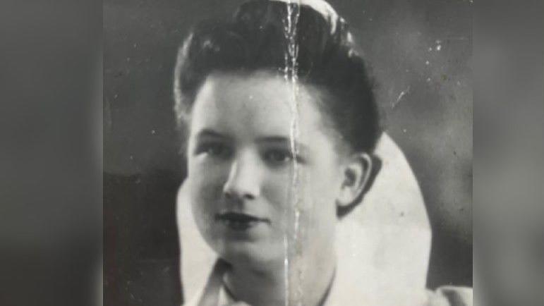 Black and white photograph showing a young woman with dark hair in a chignon and a serious expression. She is wearing a white collar, part of her nurse's uniform, which stands up behind the back of her neck.