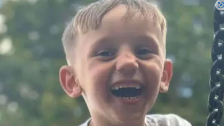 A close up of Carlos looking straight and the camera, laughing, with a blurred background of trees