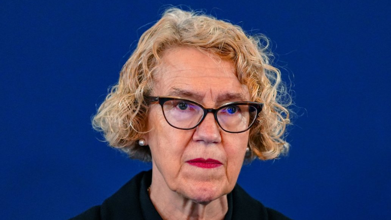 Public inquiry chair Lady Justice Thirlwall. She has curly blonde hair and wears black oval glasses. She appears in front of a dark blue backdrop.