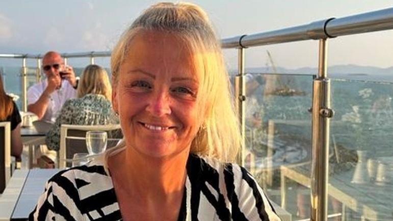 Anita Rose sitting at a table at a rooftop restaurant. She is smiling, has most of her blonde hair tied back and is wearing a black and white striped shirt/top