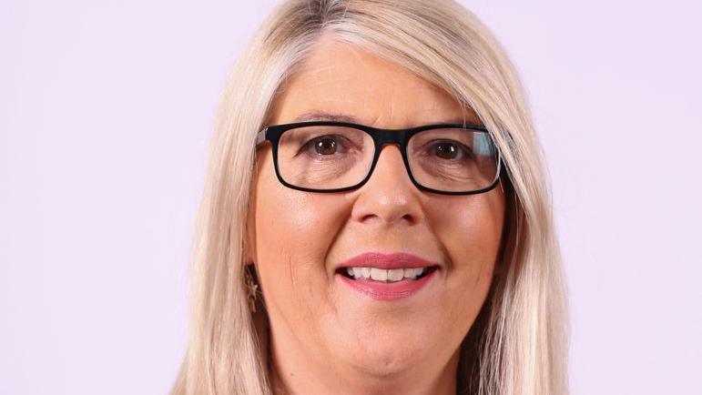 A woman with blonde hair and dark framed glasses