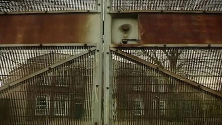 View of rusted iron security gates of the former Medomsley Detention Centre with the abandoned two storey building behind.