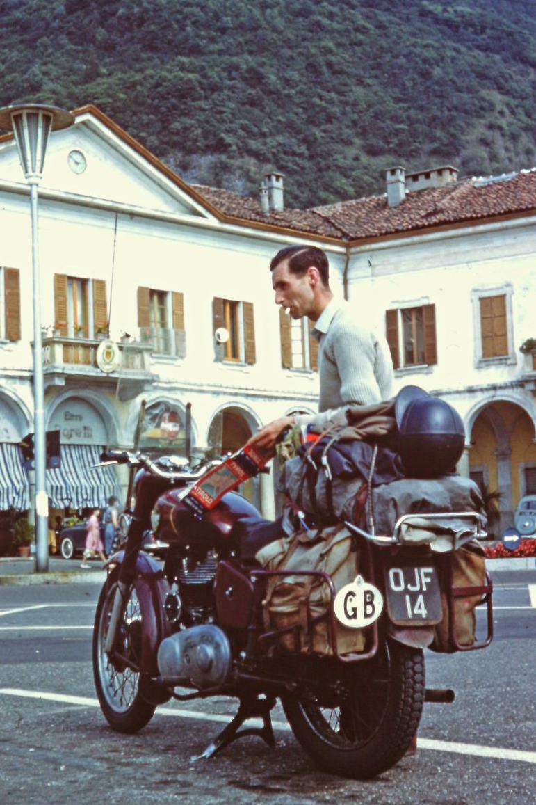 Ray Stokes with his old motorbike with a GB sign on the back, and buildings and a hillside in the background