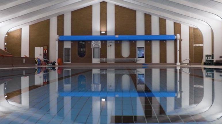 The refurbished pool has a new poolside area. Photographed before the opening, the water is still and the tiles at the bottom of the pool are clearly visible. The white columns surround the pool are lit up.