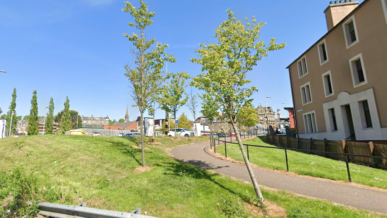 A grassy area with a path running through it and houses in the background