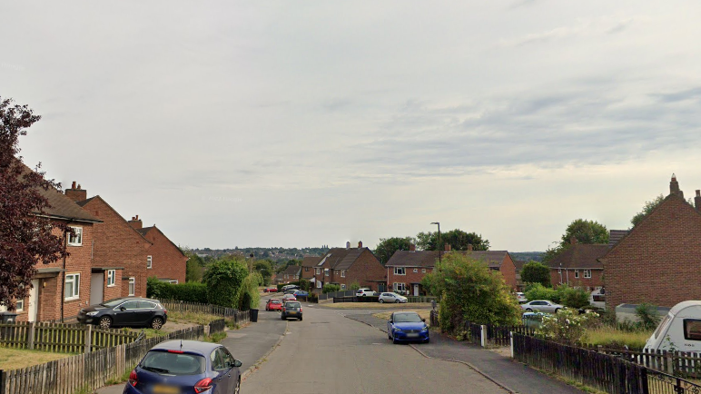 A residential street with red brick houses and cars parked on the side of the road