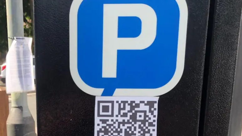 A parking machine with a large white P on a blue background with a QR code sticker below it