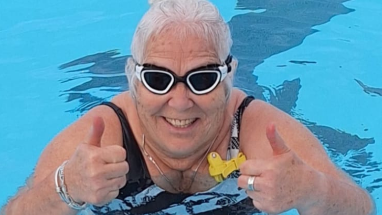 Clare Marshall is wearing a black and white swimsuit and in the water, she has goggles on and has her thumbs up to the camera.