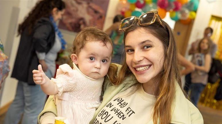 Woman in yellow smiling at the camera. She is holding a baby.