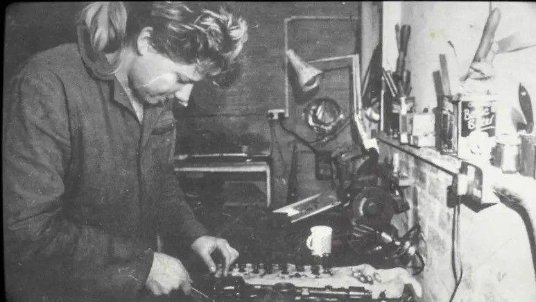 A female mechanic pores over a workbench in a monochrome picture.