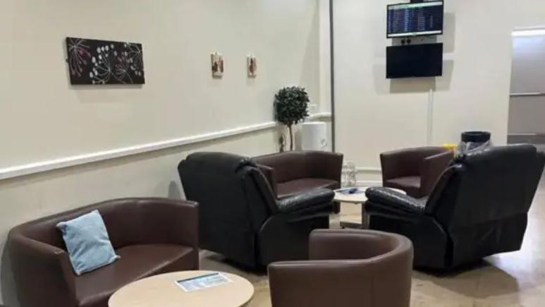 A waiting room with brown couches, tables, black leather recliners and a TV hanging on the wa