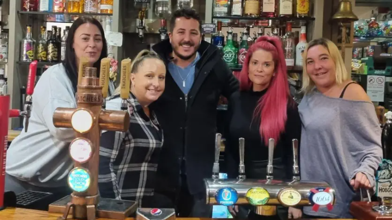 A group of people, made up of four women and one man, stand behind the bar at the Wheatsheaf Pub in Calne in Wiltshire