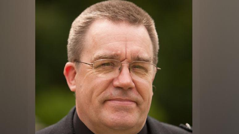 A man in his 50s wearing a jacket and white tie