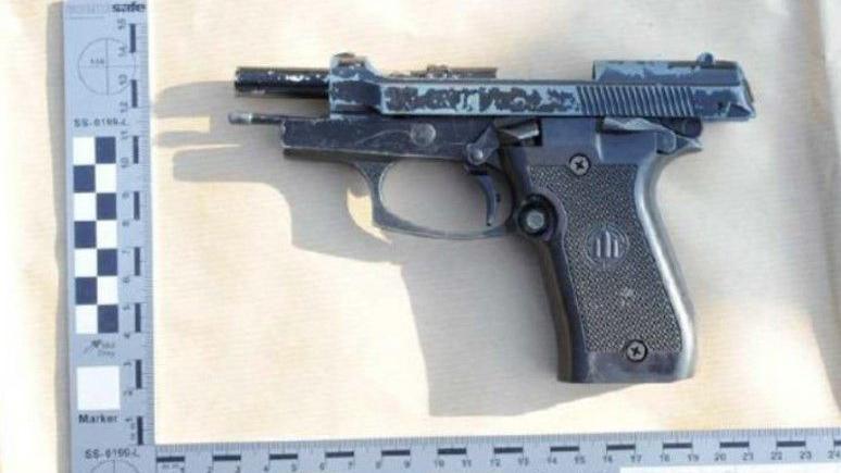 A gun, with a ruler below and above to measure its size. It is black, with metal visible as some of the paint has chipped off.