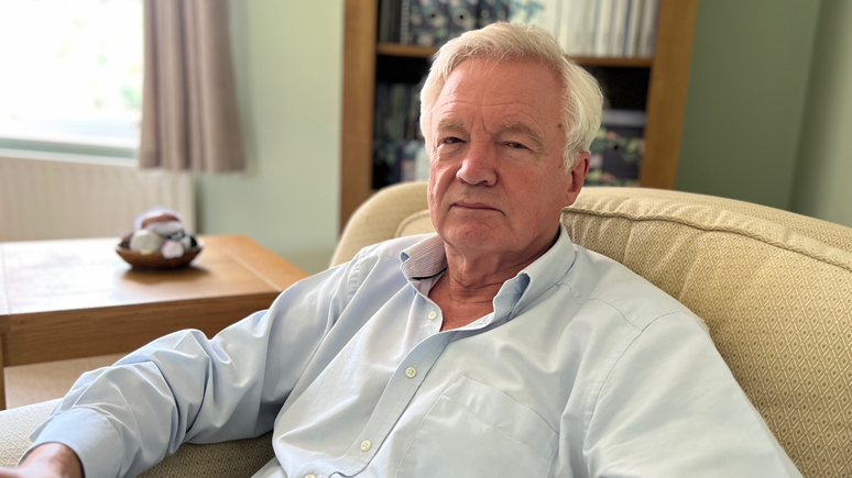 MP Sir David Davis, who has white hair and a is wearing a light blue collared shirt, pictured sitting in an armchair with a determined expression.