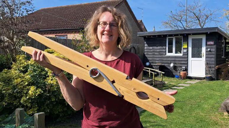a woman in a red t-shirt standing outside holding a big clothes peg