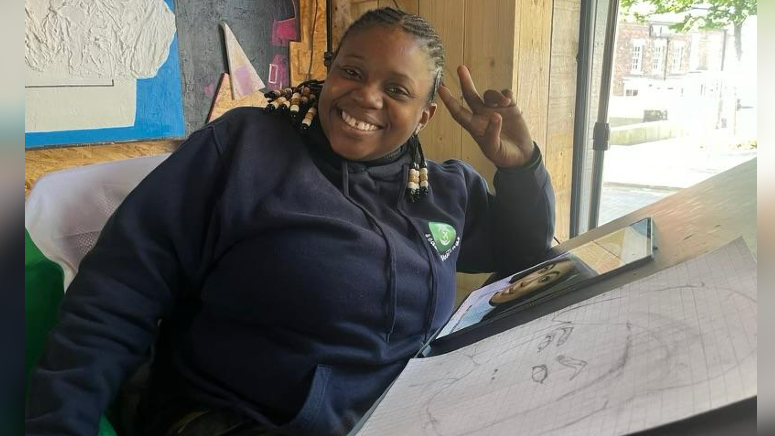 Abidemi Praise Omopariola, a black woman with braided hair, smiles while in front of her easel