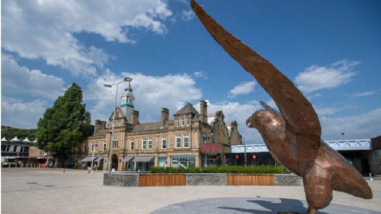 Public artwork of a large metal sculpture of bird about to take flight in the square outside Darwen Town Hall