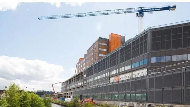 A huge new building sits by a canal. It has a crane on top of it and looks like it is still under constuction