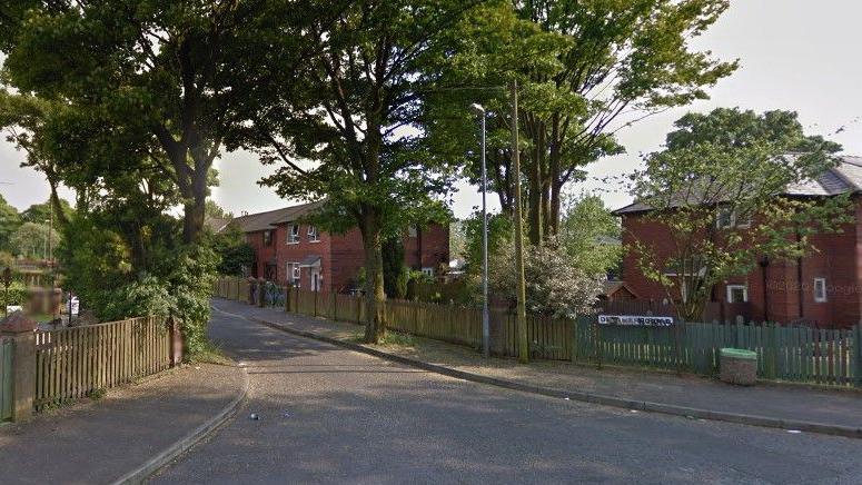 The opening of Delamere Road, where three large trees border the pavement and wooden fences stand in front of three houses