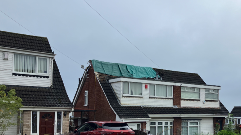 A two-storey house with green tarpaulin draped over the roof where it was damaged by lightning.