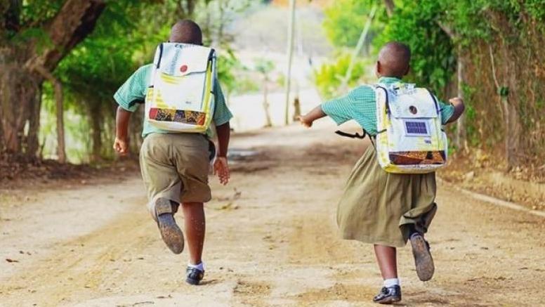 Two children running down a road with backpacks on