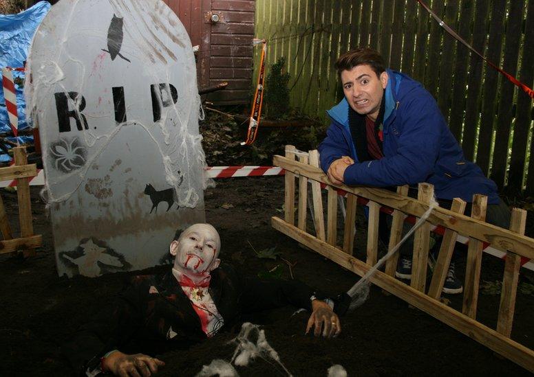 Ricky stands next to a grave with a dead person in it