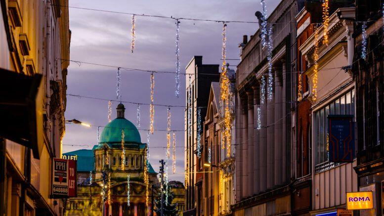 Illuminated Christmas decorations strung between buildings, with the green-domed city hall in the background.