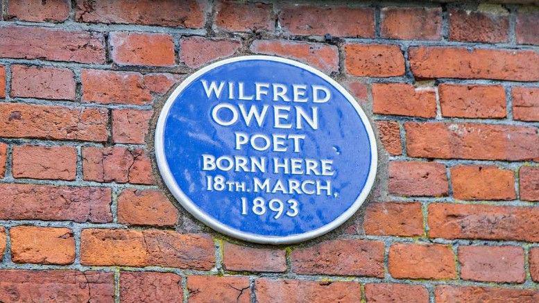 A blue plaque on a brick wall that reads "Wilfred Owen, poet, born here, 18th March, 1893"