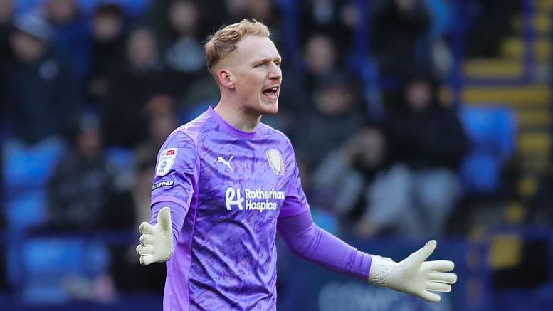 Cameron Dawson, playing in a purple shirt of Rotherham, shouts at his defence