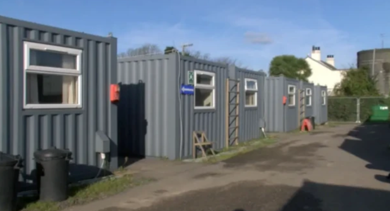 Four navy blue corrugated iron shipping containers with windows. 