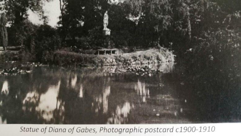 An old black and white picture of a statue on an island surrounded by water.