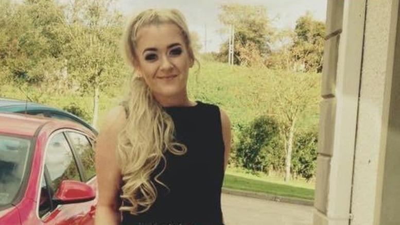 It shows Caoimhe O'Brien wearing a black top standing beside a red car