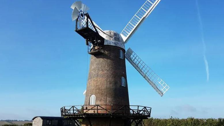 The red brick windmill with white sails under a bright blue sky