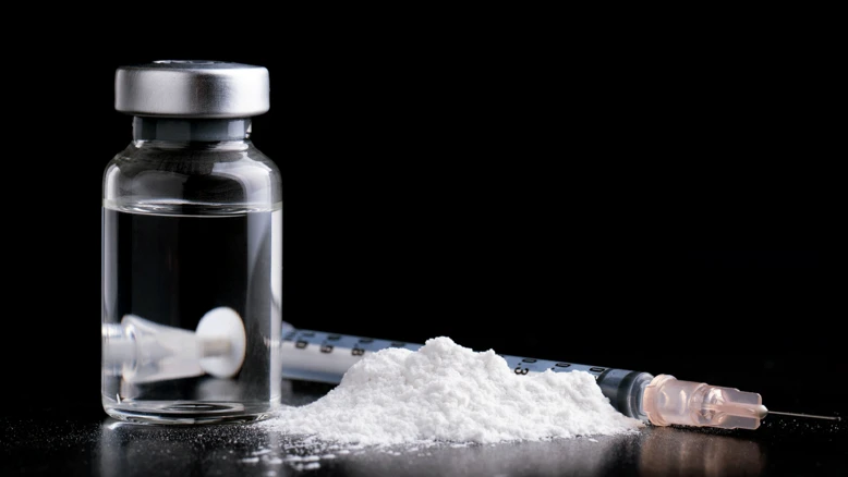 A small bottle of ketamine and syringe on a table with a black background.