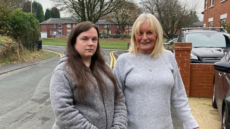 Michelle Kight, wearing a grey hoodie, and Denise Murphy, wearing a grey jumper, stand together in front of the new double yellow lines on Major Street in Milnrow.