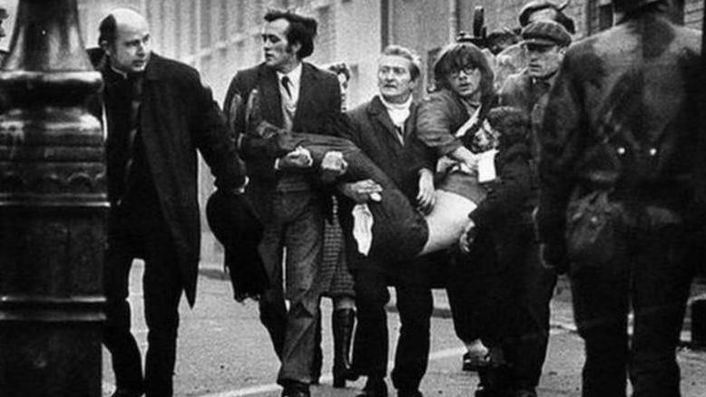 An iconic image of Bloody Sunday in which a group of men carry one of the injured through the streets. A priest walks ahead and  waves a white handkerchief