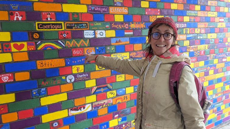 Fraisia in front of a mural, pointing towards it and smiling to camera