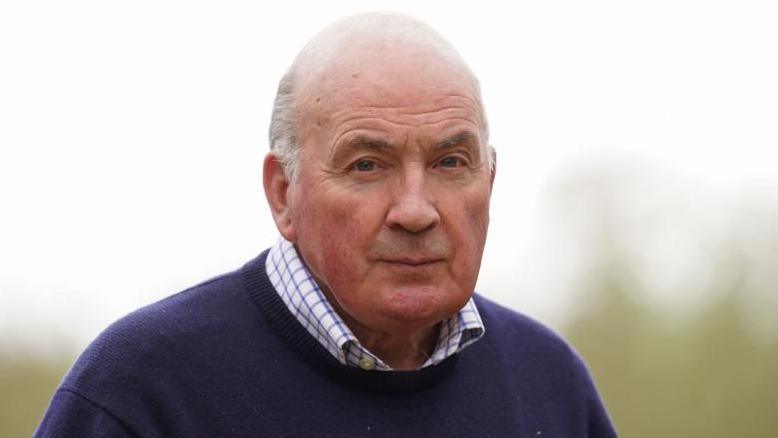 A headshot of Lord Dannatt, wearing a shirt and navy blue jumper