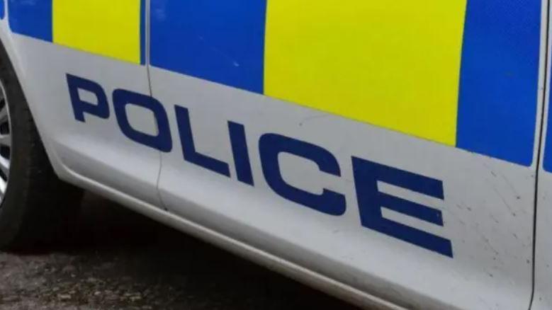 Close-up of the side of a police vehicle showing part of the yellow and blue police pattern and saying the word 'police' in blue capital letters