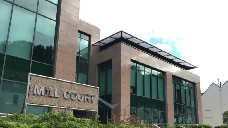 A modern office building made of red granite and glass, with a sign saying Mill Court.