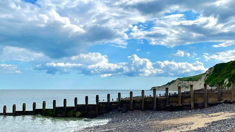 A pebble beach meeting the sea with blue skies above